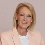 Professional headshot of Karen King, senior executive in a light peach blazer with short blonde hair, smiling confidently.